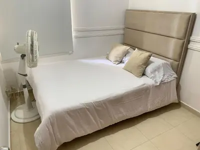 a bed with white sheets and pillows next to a fan at Habitación en Villa Carolina con aire in Barranquilla