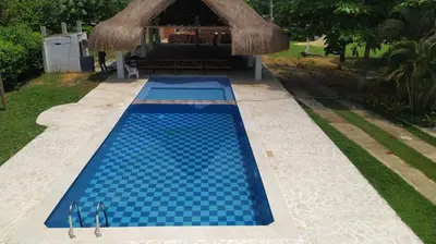 a blue swimming pool with a thatched roof and a resort at Casa Campestre Rancho 75 Eco Park in Arjona