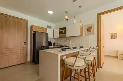 a kitchen with a counter with stools and a refrigerator at Mágico Oasis en Baia Kristal Vista a la Laguna 2BR in Los Arrayanes