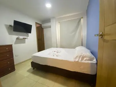 a bedroom with a bed with white sheets and a tv at Hotel Prado Cartagena in Cartagena de Indias
