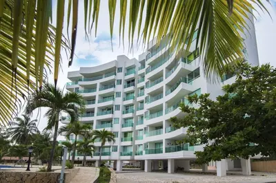 a large white building with palm trees in front of it at Magico Apartamento Frente al Mar 3 Habitaciones MSC22 in Coveñas