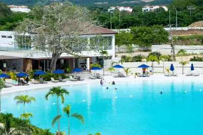 a large swimming pool with palm trees and blue umbrellas at Apartamento con piscina, playa y cerca aeropuerto de Cartagena in Cartagena de Indias