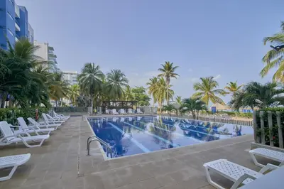 a swimming pool with white chairs and palm trees at Hermoso Apartamento Frente al Mar 2 Habitaciones PAZ127 in Coveñas