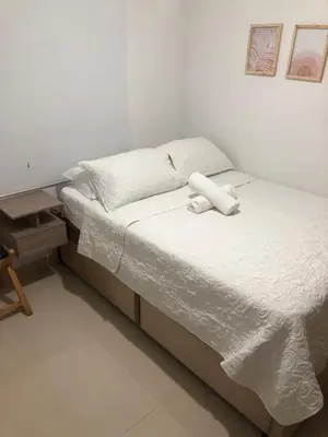 a bedroom with a bed with white sheets and a table at Comfortable 2 bedroom apartment with pool in Miramar in Barranquilla