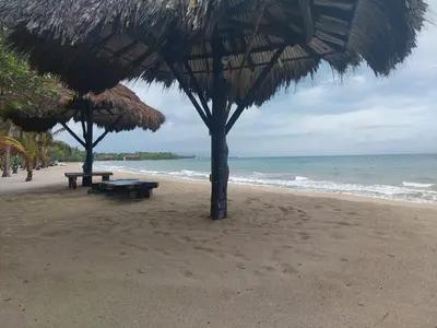 a beach with two picnic tables and a straw umbrella at Cabaña frente al mar en la playa del Calao in San Antero