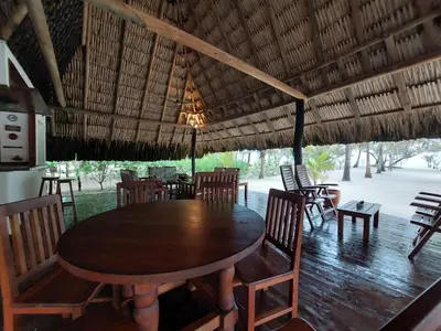 a large wooden table and chairs under a straw roof at Cabaña frente al mar en la playa del Calao in San Antero