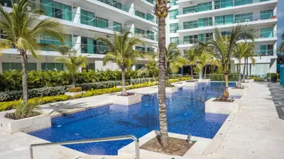 a swimming pool with palm trees in front of a building at Morros Ultra, Beachfront & 2 Bedrooms by Inmobiliaria MFR in Cartagena de Indias