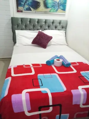 a bed with a red and white blanket with slippers on it at Hostal Costacaribeam in Barranquilla