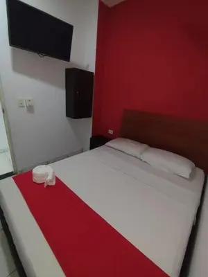 a bedroom with a white bed with a red wall at Hotel Madeleine Inn Sede Sur in Barranquilla