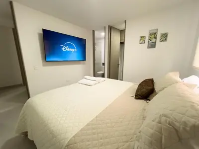 a bedroom with a large white bed with a tv on the wall at 2 cuartos AC y piscina in Cartagena de Indias