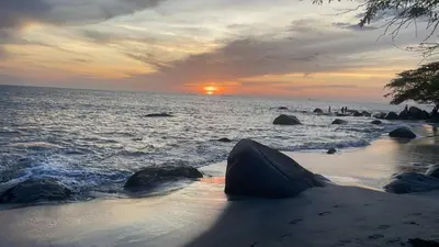 a sunset on a beach with rocks in the water at Maranta Beach in Santa Marta