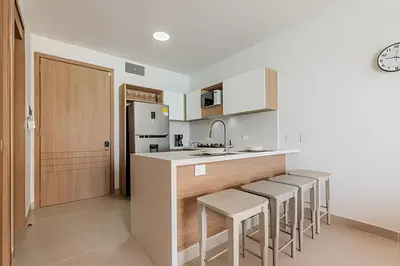 a kitchen with white cabinets and a counter with stools at Espectacular vista a laguna de Kristal / 1 alcoba in Los Arrayanes