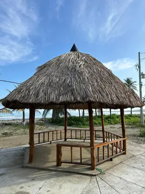 a bench under a straw hut on the beach at Ibiza beach in Moñitos