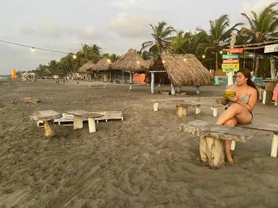a woman sitting on a bench on the beach at Refugio olgamar, Cabaña con kiosco cerca al mar in Moñitos
