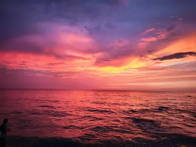 a sunset over the ocean with a person on the beach at Modern suite steps from the sea in Santa Marta