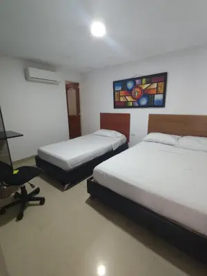 a bedroom with two beds and a desk and a chair at Hotel Madeleine Norte in Barranquilla
