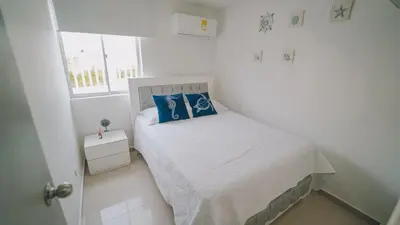 a small white bedroom with a bed with blue pillows at Azul Caribe 104 in Coveñas