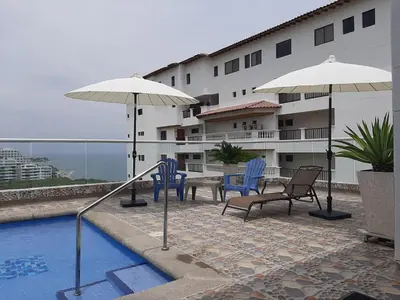 a pool with chairs and umbrellas next to a building at Apartamento con vista al mar en Bello Horizonte, Santa Marta in Santa Marta
