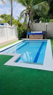 a swimming pool with green grass next to a house at Casa a 2 minutos de la playa en playa mendoza in Tubará