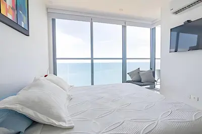 a bedroom with a white bed with a large window at Espectacular Apto Piso 21 de 2 Hab - Morros City in Cartagena de Indias