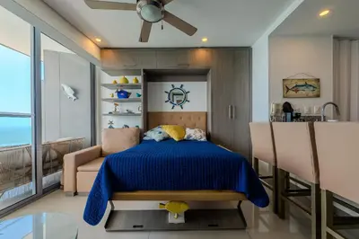a bedroom with a blue bed and a kitchen at Piso 27 - Espectacular apartamento en Bocagrande in Cartagena de Indias
