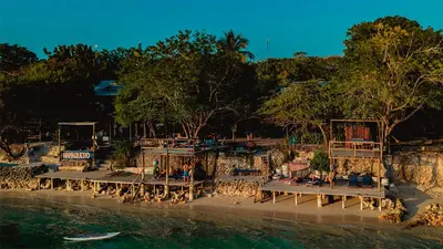 a group of people sitting on benches next to the water at El Hamaquero Hostal EcoNativo in Isla Grande