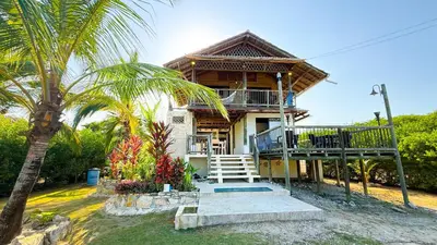 a house with a balcony and a palm tree at Cabaña Punta Helvetica in San Antero