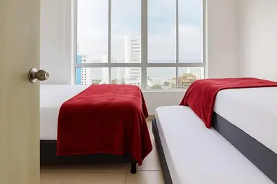 two beds with red sheets in a room with a window at Cartagena near the historic center and beaches in Cartagena de Indias