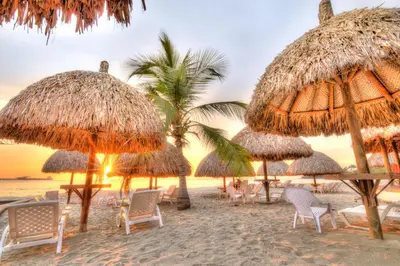a group of straw umbrellas and chairs on a beach at Hotel Santorini Casablanca Resort in Santa Marta
