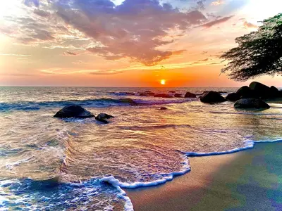 a sunset on the beach with rocks in the water at Aqua Marine Suite - Santa Marina Condo in Santa Marta