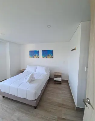 a white bedroom with a large bed and two paintings at Oceani Tower Cielo Mar Apartment in Cartagena de Indias