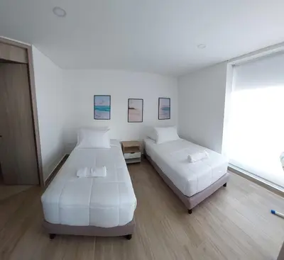two beds in a room with white walls and wood floors at Oceani Tower Cielo Mar Apartment in Cartagena de Indias