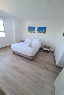 a white bedroom with a bed and a wooden floor at Oceani Tower Cielo Mar Apartment in Cartagena de Indias