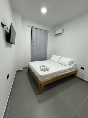 a white bedroom with a bed with a tv on the wall at Hotel Portón de La Sabana in San Onofre