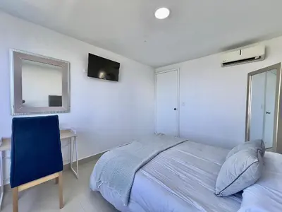 a bedroom with a bed and a chair and a mirror at Apartamento con vista al mar - Riviera Mulata Beach in Cartagena de Indias