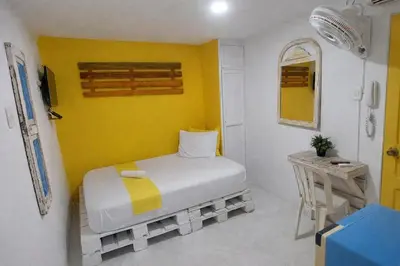 a small room with a bed and a yellow wall at QuillaHost Guesthouse in Barranquilla