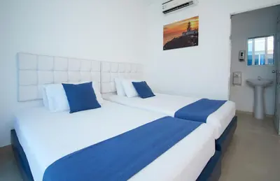 two white beds with blue pillows in a room at Palma Linda Coveñas by Bernalo Hotels in Coveñas