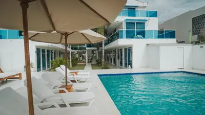 a swimming pool with white chairs and an umbrella and a building at Palma Linda Coveñas by Bernalo Hotels in Coveñas