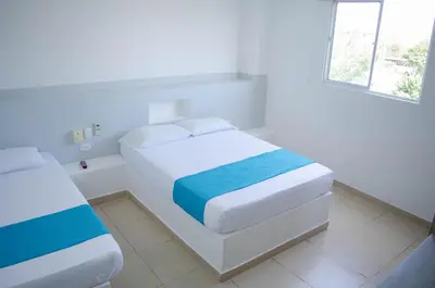 a white bedroom with two beds and a window at Hotel Sofichic Barranquilla in Barranquilla