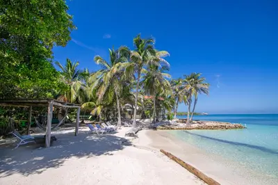 a beach with chairs and palm trees and the ocean at Cabana SalSiPuedes in Tintipan Island