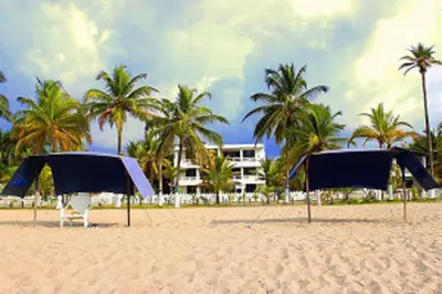 two umbrellas on a sandy beach with palm trees at Apartamentos Las Múcuras in Coveñas