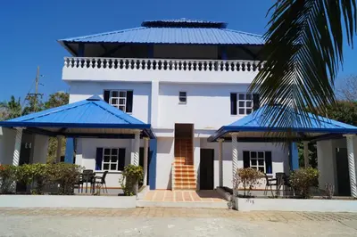 a white house with blue roofs and a palm tree at Condominio Punta Bolivar in San Antero