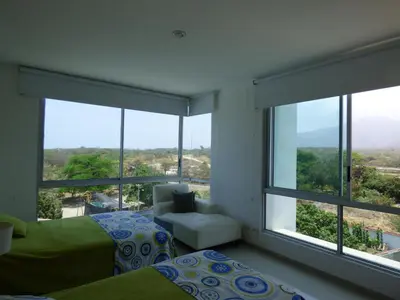 a bedroom with a bed and a chair and windows at Costa Azul Suites 401 in Santa Marta