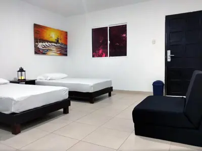 a room with two beds and a couch and a chair at Hotel El Emigrante in Puerto Colombia