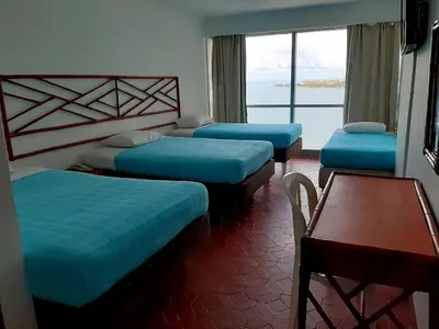 a room with three beds and a table and a window at Hotel Costa del Sol in Cartagena de Indias