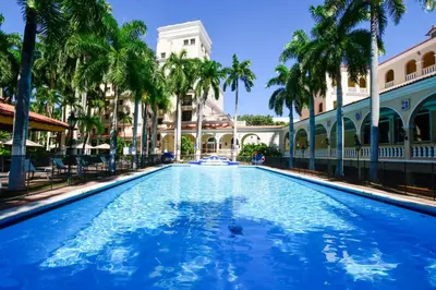 a swimming pool with palm trees in front of a building at Hotel El Prado in Barranquilla