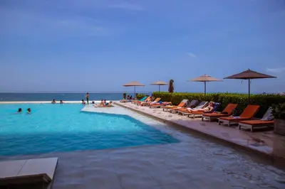 a swimming pool with chairs and umbrellas and the ocean at 41st Fl Beach Condo in Bocagrande in Cartagena de Indias