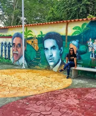 a woman sitting on a bench in front of a mural at Casa Turística Realismo Mágico in Aracataca