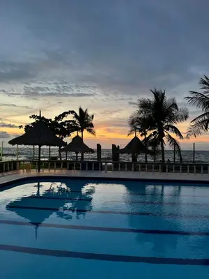 a swimming pool with palm trees and the ocean at sunset at Alquiler casa en la playa, Tolu in Tolú