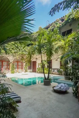 a swimming pool with palm trees and a building at Hotel Boutique Casa Del Arzobispado in Cartagena de Indias